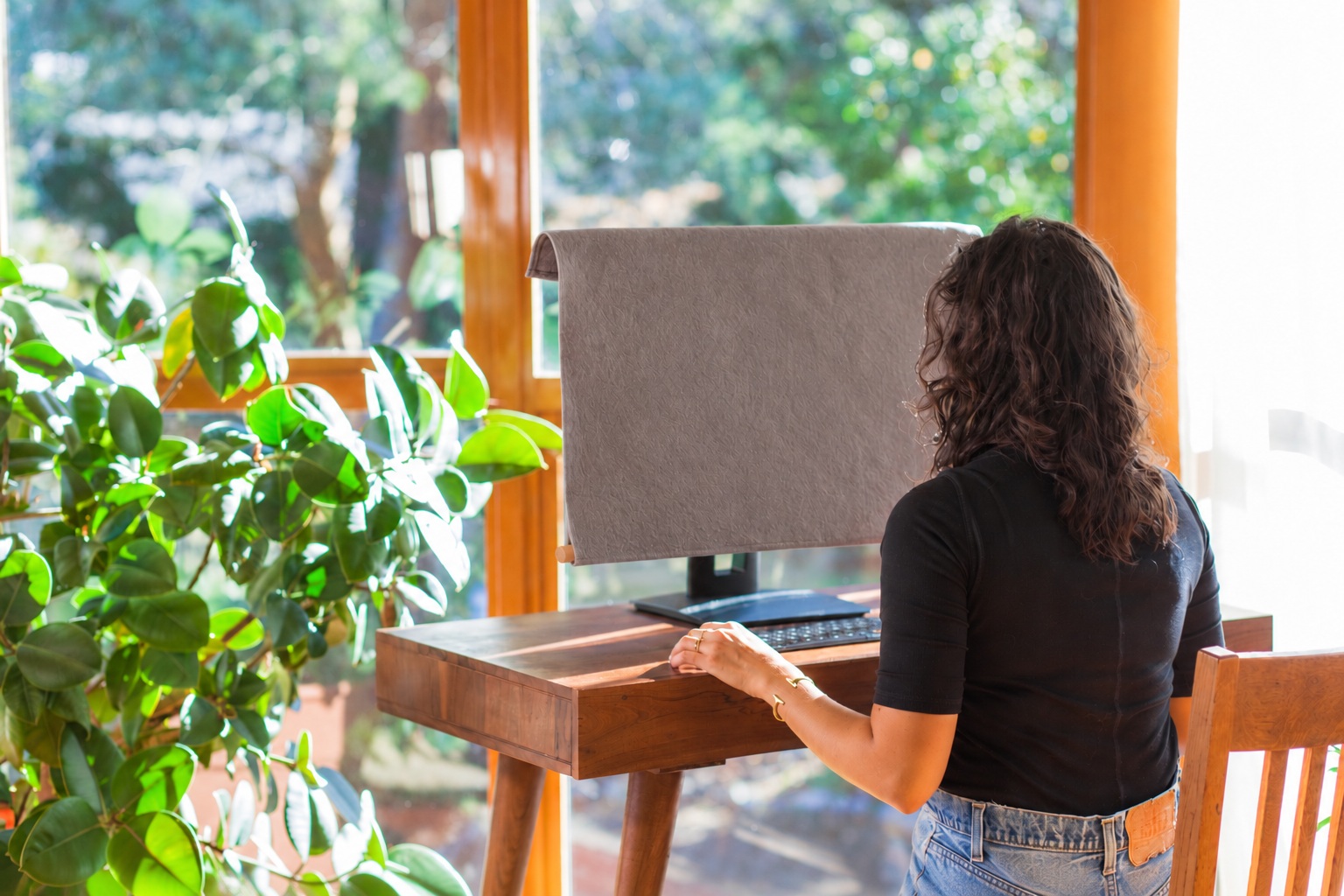 Edited concept photograph of a grey Lona monitor cover with a wooden dowel concealed in its hem in a sunny home office