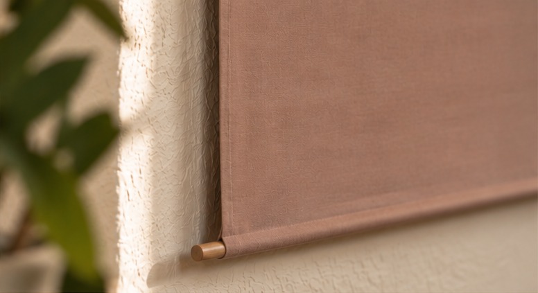 Close-up of the dusty rose Lona fabric cover and wooden dowel against textured plaster